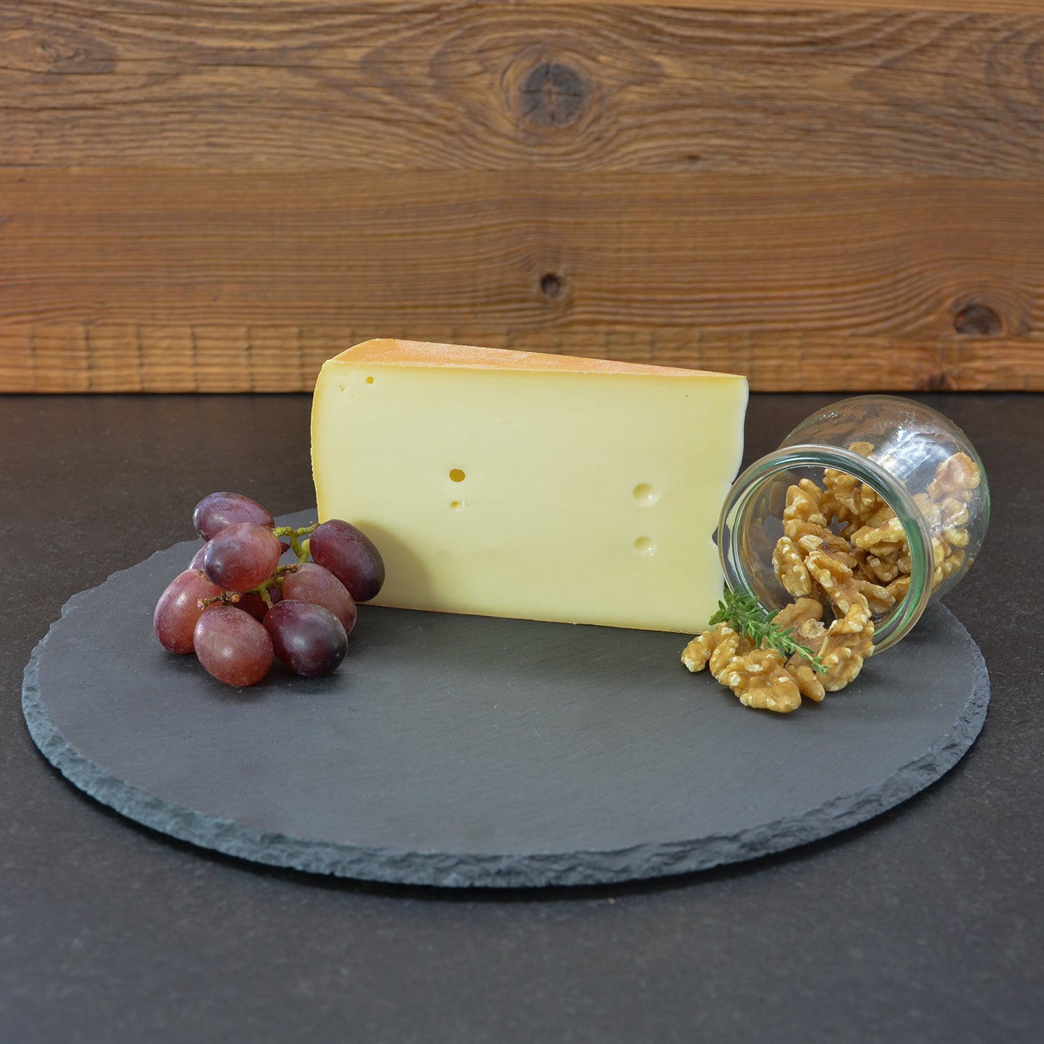 Stück Almkäse von vorne, umgeben von Walnüssen und Weintrauben