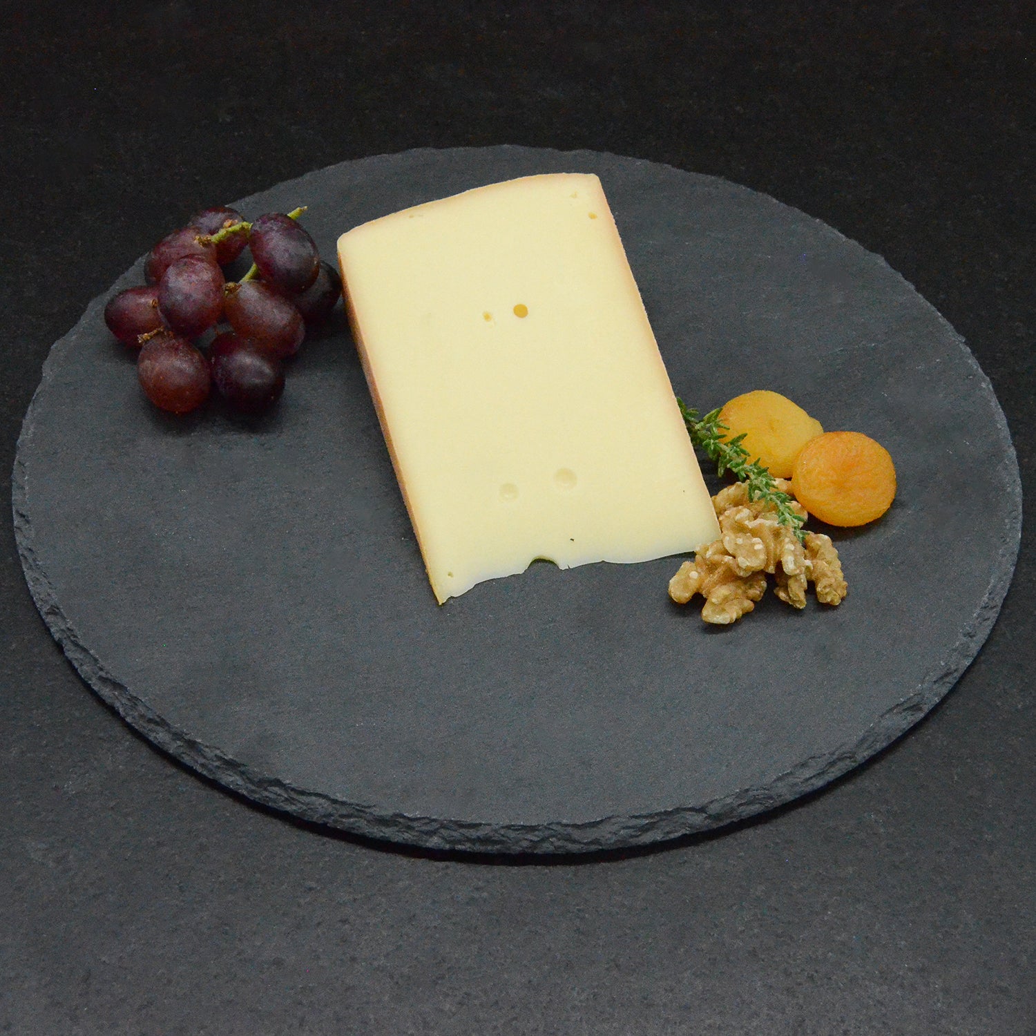 Stück Almkäse von oben, dekoriert mit Walnuss, Marille und Weintrauben